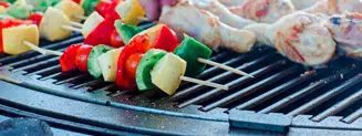 Vegetable skewers and chicken legs being cooked on a gather grill