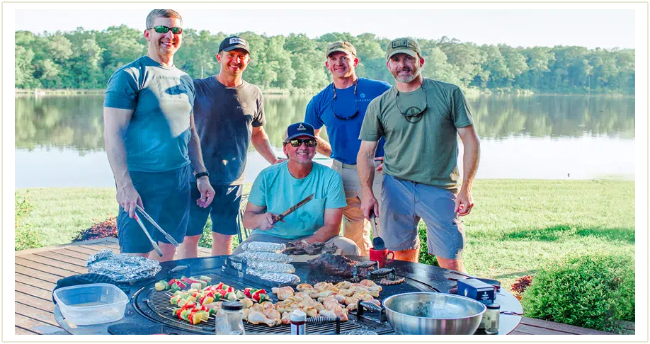 Five men standing by a large circular Gather Grill which is loaded up with vegetarian and chicken skewers as well as barbeque. To the left there is a separate image of the gather grill unoccupied.
