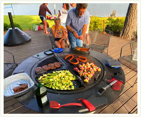 A man cooking sausages, skewers, steak and a variety of vegetables on a gather grill