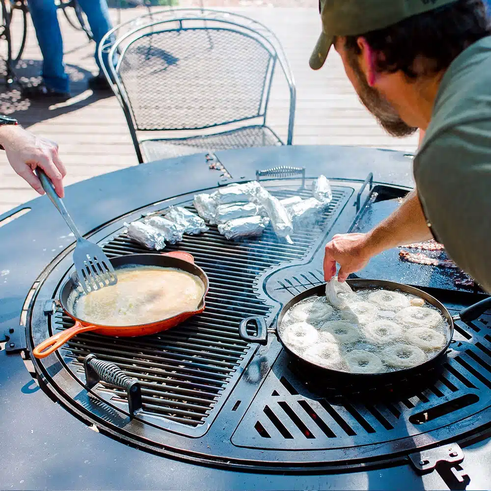 A gather grill combo loaded with a variety of food wrapped in foil, being tended to by two men.