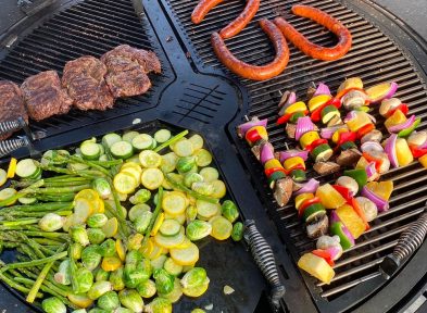 A variety of vegetables and hotdogs being cooked on a gather grill