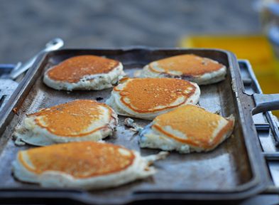 Several pancakes being cooked in a cast iron skillet on a grill